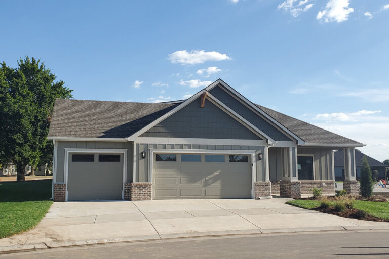 Exterior of ranch home. The paint is tan and there is a three car garage.